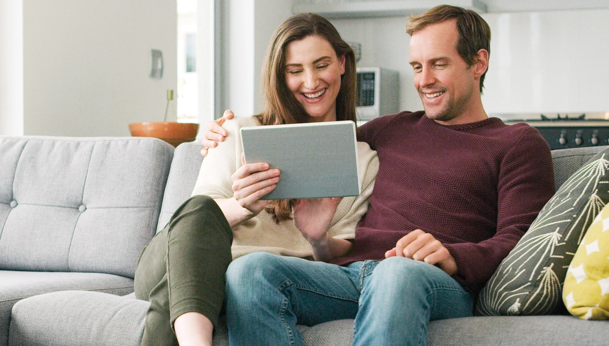 couple-on-the-couch-looking-at-tablet-1200x683.webp