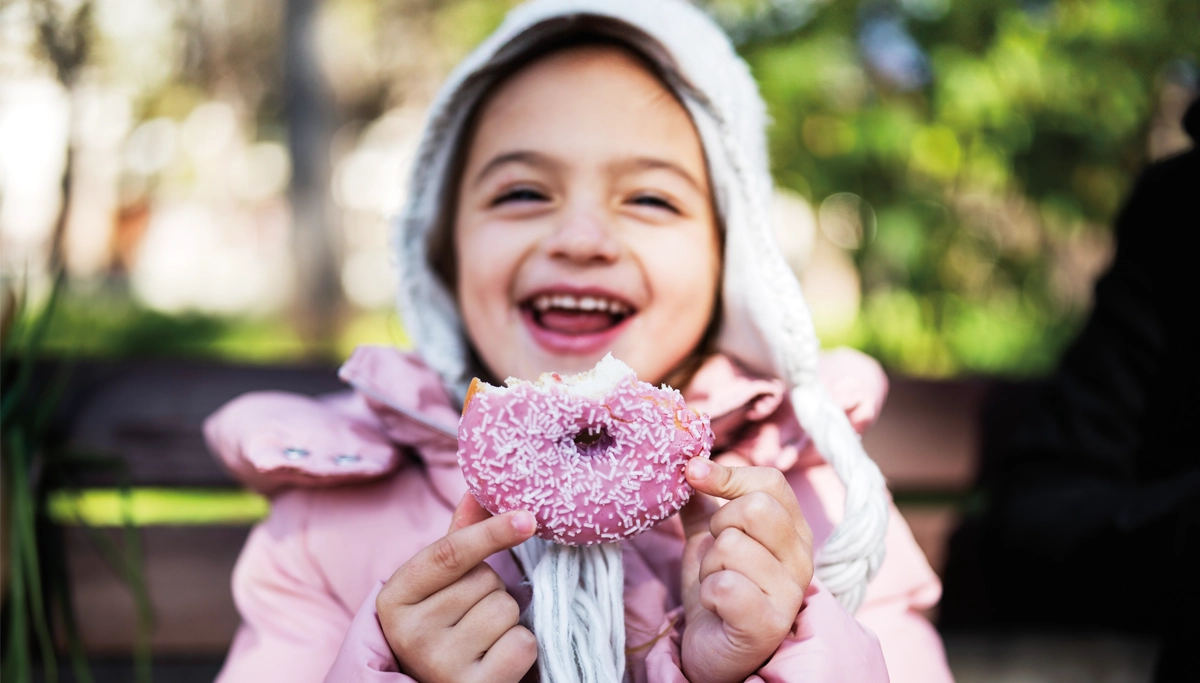 young-girl-smiling-with-a-donut-1200x683.webp