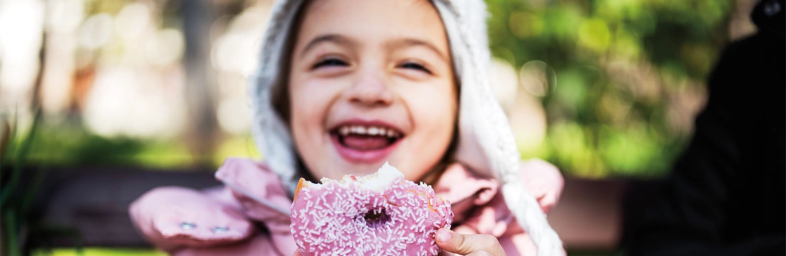 young-girl-smiling-with-a-donut-1600x522.webp