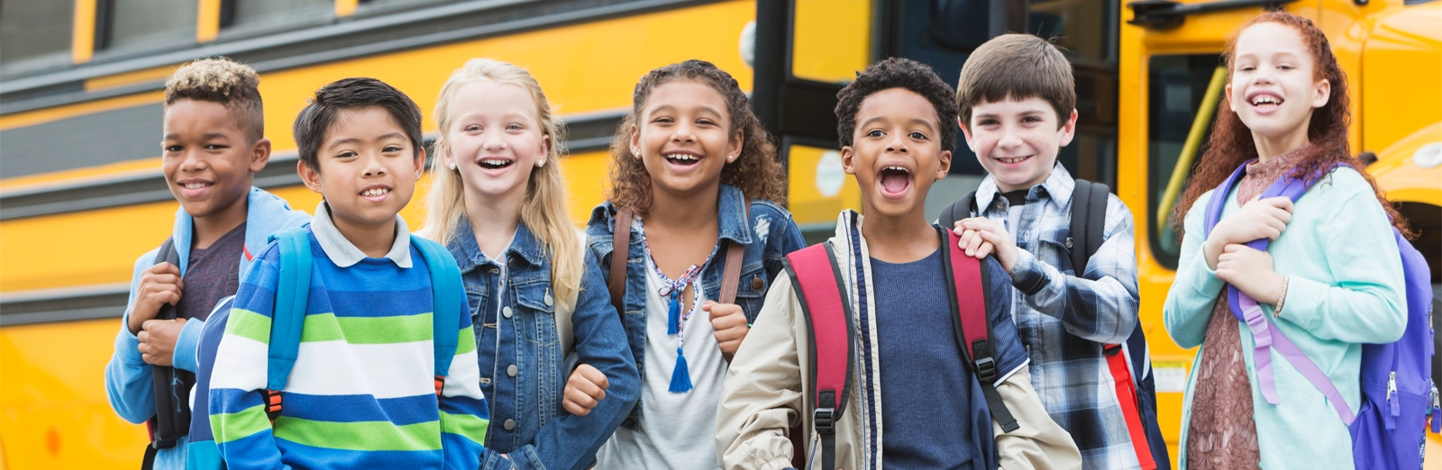 young-students-smiling-by-school-bus-1600x522.webp