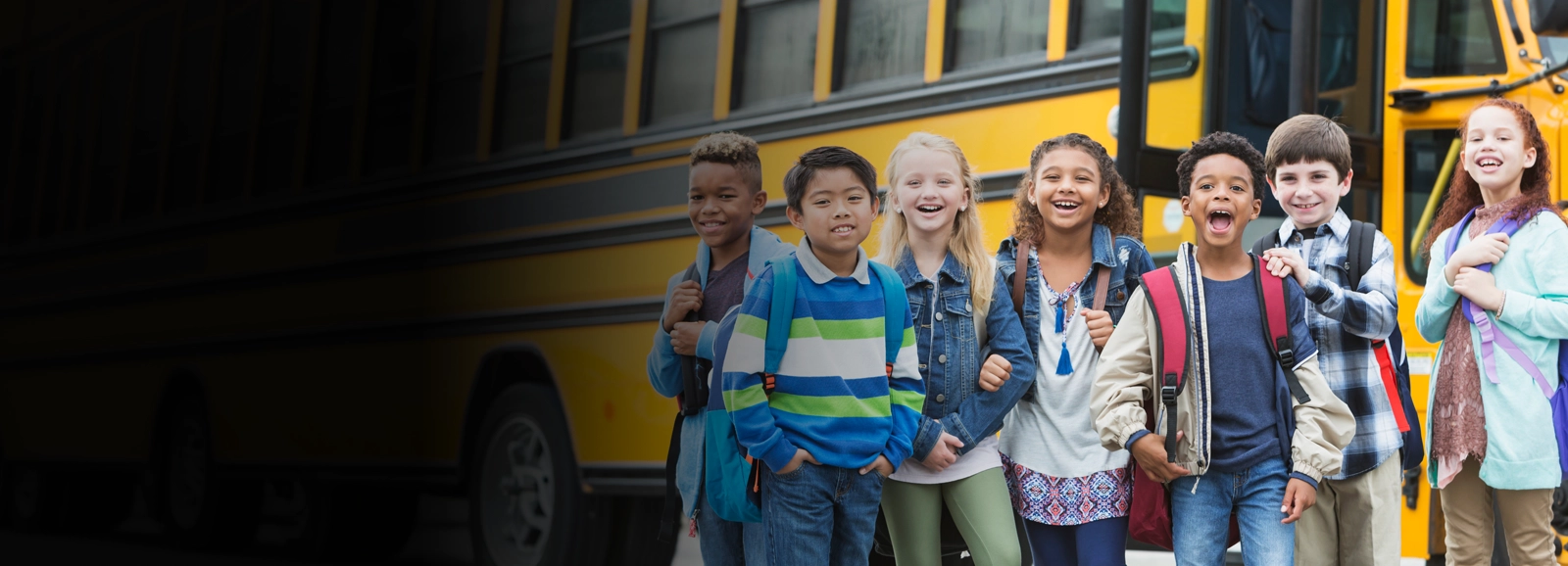 young-students-smiling-by-school-bus-1600x578.webp