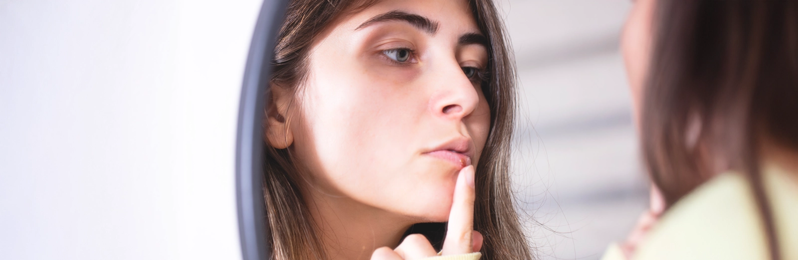 woman-looking-at-cold-sore-in-mirror-1600x522.webp